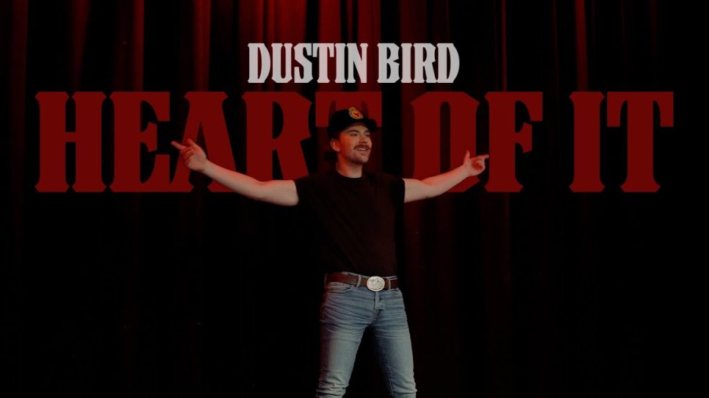 Dustin Bird - "The Heart of It" - YouTube music video thumbnail with the artist standing, arms outstretched, highlighting the song title.